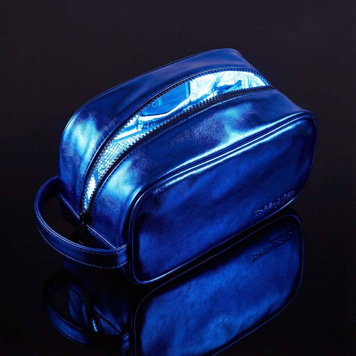 Ocean blue metallic LED travel makeup bag with illuminated interior on reflective black surface. Large vegan leather cosmetic organizer with rechargeable lighting and wipeable insulated lining by Thread Original. 