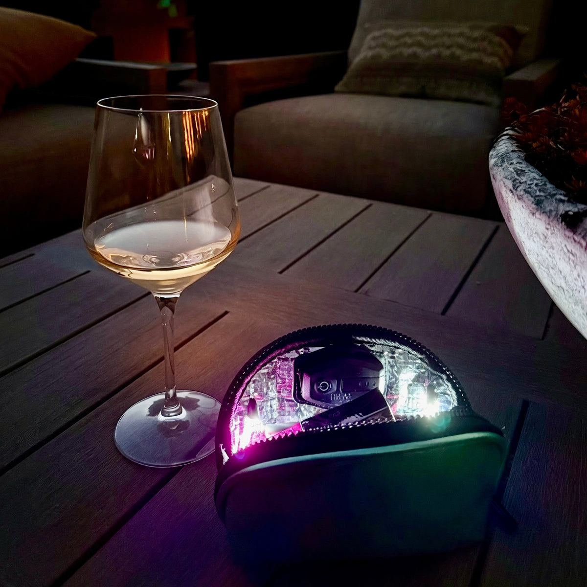 Luna LED makeup bag illuminating cosmetics on an outdoor table at sunset beside a wine glass.
