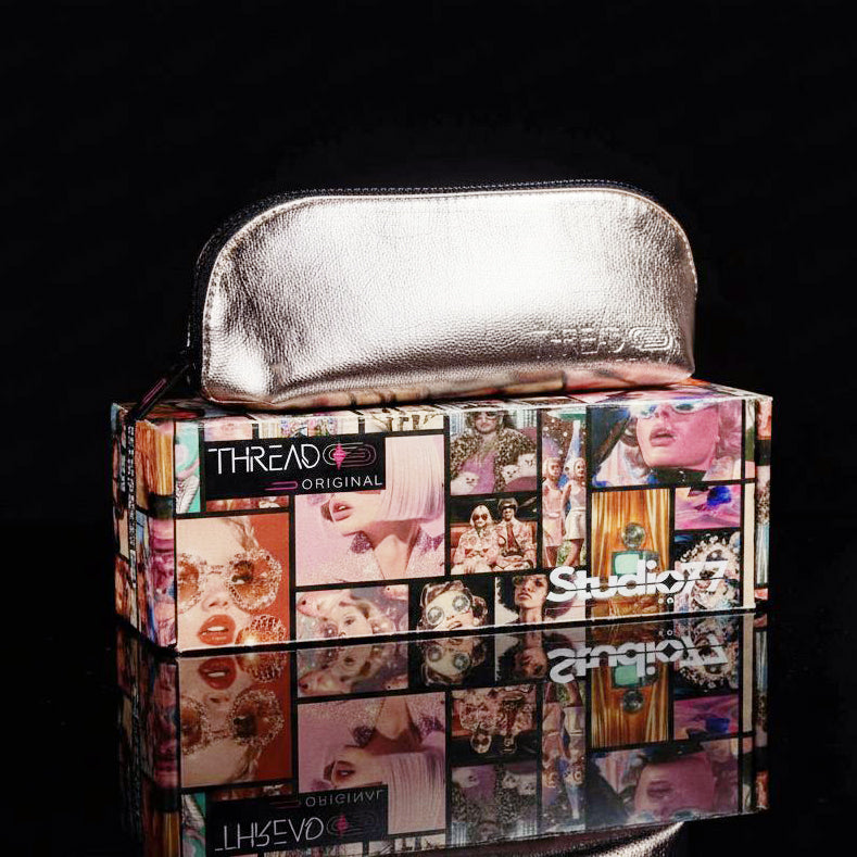 Lyra compact makeup bag in Fizz metallic champagne, closed and resting on Thread Original packaging.