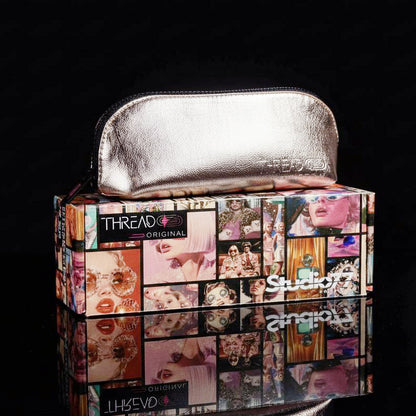 Lyra compact makeup bag in Fizz metallic champagne, closed and resting on Thread Original packaging.