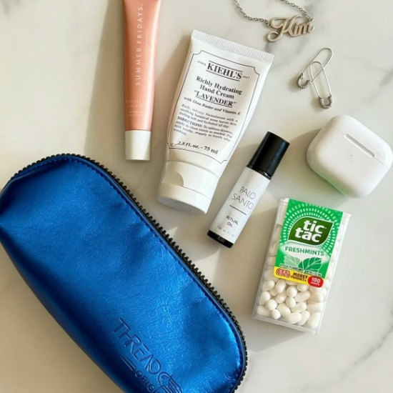 Ocean blue Lyra compact makeup bag styled with everyday essentials including lip balm, hand cream, mints, jewelry, Air pods and a fragrance roller.